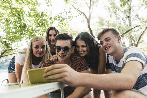 Gruppe von glücklichen Freunden, die im Freien auf ihr Handy schauen - UUF14859