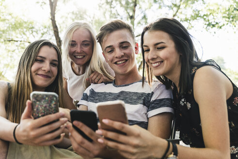 Gruppe lächelnder Freunde, die im Freien auf ihre Handys schauen - UUF14864