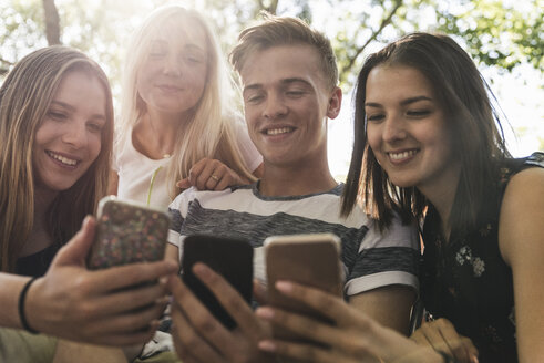 Gruppe lächelnder Freunde, die im Freien auf ihre Handys schauen - UUF14865
