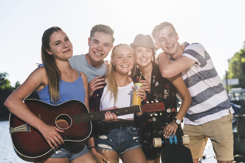 Porträt einer Gruppe von glücklichen Freunden mit Gitarre am Flussufer, lizenzfreies Stockfoto