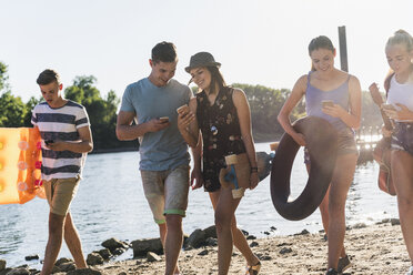 Gruppe von Freunden mit Handys beim Spaziergang am Flussufer - UUF14896