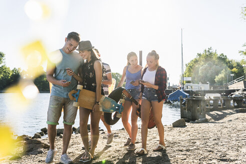 Group of happy friends with cell phones walking at the riverside - UUF14898