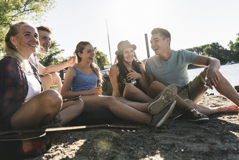 Eine Gruppe glücklicher Freunde sitzt mit Getränken am Flussufer - UUF14900