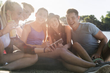 Group of happy friends sitting outdoors with drinks and cell phone - UUF14901