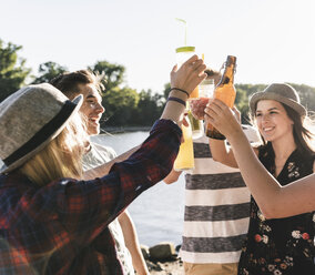 Eine Gruppe glücklicher Freunde steht am Flussufer und stößt mit Getränken an - UUF14906