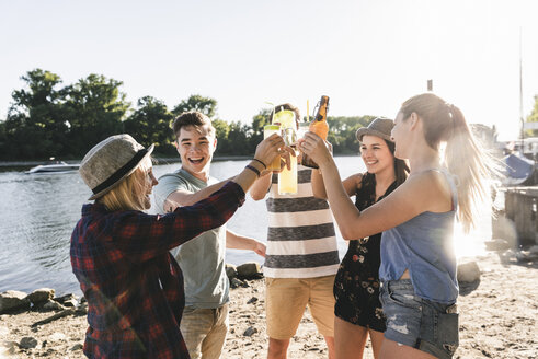 Eine Gruppe glücklicher Freunde steht am Flussufer und stößt mit Getränken an - UUF14907