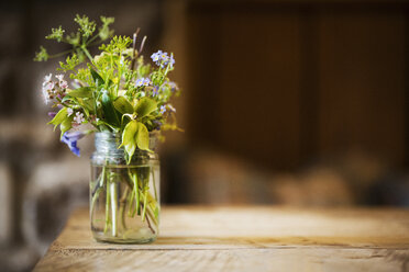 Nahaufnahme eines Glasgefäßes mit einem kleinen Strauß Wildblumen auf einem Holztisch. - MINF04401