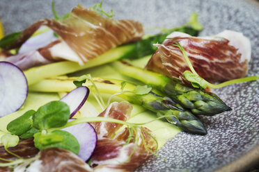 Close up high angle view of green asparagus and ham on a plate. A restaurant dish. - MINF04410