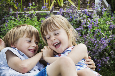 Ein lächelnder Junge und ein lächelndes Mädchen, die zusammen im Freien in einem Garten spielen. - MINF04422