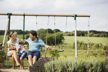 Man, woman and boy sitting side by side on a swing in a garden. - MINF04435