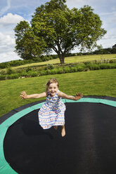 Mädchen im Sommerkleid springt auf einem Trampolin in einem Garten. - MINF04436