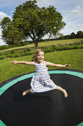 Mädchen im Sommerkleid springt auf einem Trampolin in einem Garten. - MINF04437