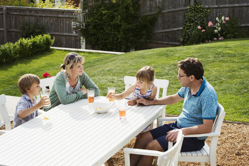 Eine Familie sitzt um einen Gartentisch, Eltern und zwei Kinder, ein Junge und ein Mädchen. - MINF04438