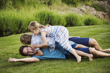 A man lying on the grass with his two children lying on top of him, playing. - MINF04444