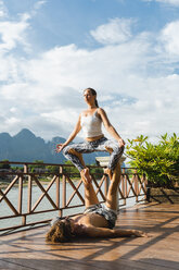 Laos, Vang Vieng, Young couple doing acro-yoga on a terrace - AFVF01221