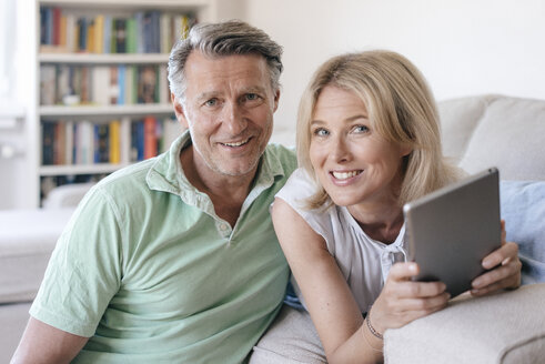 Porträt eines lächelnden reifen Paares zu Hause mit Tablet - JOSF02442