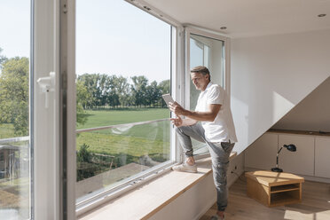 Älterer Mann mit Tablet am Fenster in leerem Raum - JOSF02443