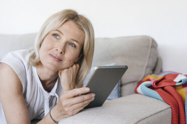 Portrait of mature woman lying on couch at home holding tablet - JOSF02444