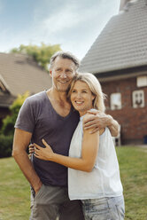 Porträt eines lächelnden reifen Paares, das sich im Garten seines Hauses umarmt - JOSF02445