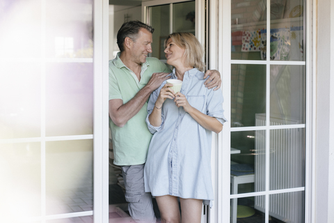 Glückliches reifes Paar am französischen Fenster stehend, lizenzfreies Stockfoto