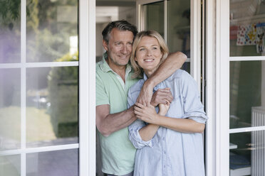 Happy mature couple hugging at French window - JOSF02466