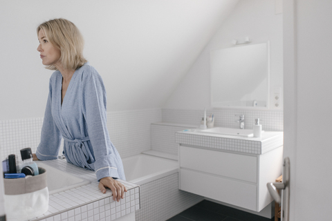 Ernsthafte reife Frau schaut in den Badezimmerspiegel, lizenzfreies Stockfoto