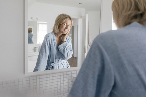 Porträt einer lächelnden reifen Frau, die in den Badezimmerspiegel schaut, lizenzfreies Stockfoto