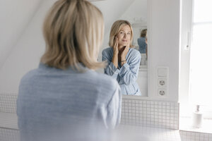 Reife Frau schaut in den Badezimmerspiegel - JOSF02486