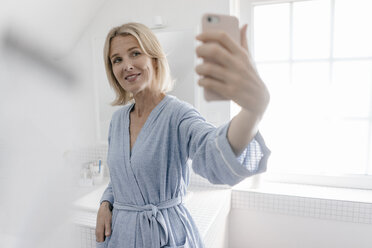 Smiling mature woman taking a selfie in bathroom - JOSF02487