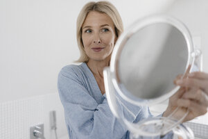 Reife Frau schaut in Schönheitsspiegel im Badezimmer - JOSF02491
