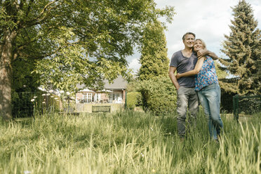 Lächelndes reifes Paar, das sich im Garten seines Hauses umarmt - JOSF02498