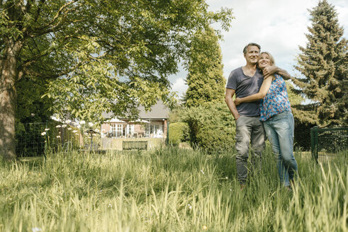 Smiling mature couple embracing in garden of their home - JOSF02498