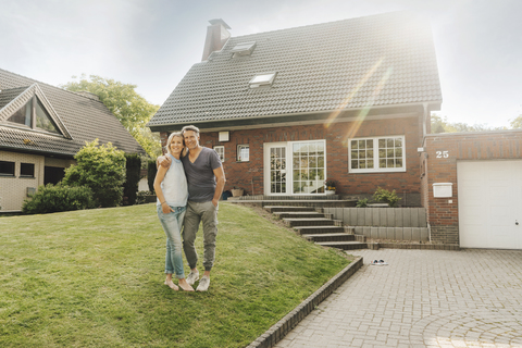 Lächelndes reifes Paar, das sich im Garten seines Hauses umarmt, lizenzfreies Stockfoto