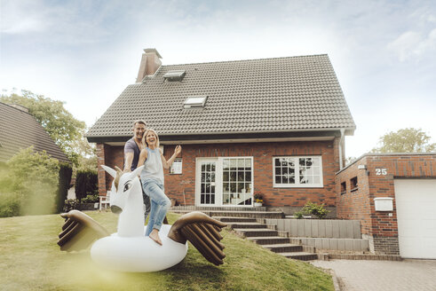 Happy mature couple with inflatable pool toy in garden of their home - JOSF02511