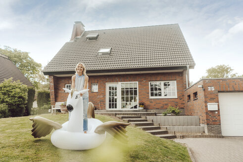 Portrait of smiling mature woman with inflatable pool toy in garden of her home - JOSF02512