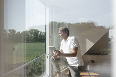 Mature man using tablet at the window - JOSF02516