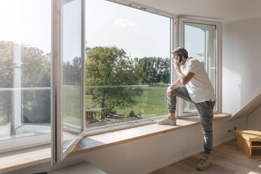 Mature man on the phone at the window in empty room - JOSF02517