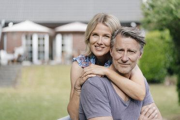 Porträt eines lächelnden reifen Paares, das sich im Garten seines Hauses umarmt - JOSF02523