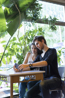 Junges Paar sitzt am Tisch und benutzt ein Mobiltelefon - AFVF01237