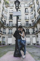 Frankreich, Paris, junges verliebtes Paar an einer Straßenlaterne vor einem städtischen Gebäude stehend - AFVF01240