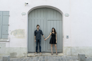 Young couple standing hand in hand in front of building - AFVF01260