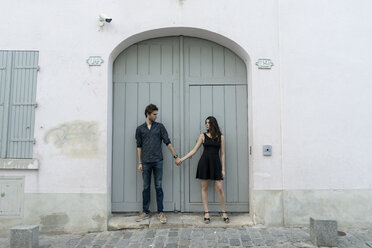 Young couple standing hand in hand in front of building - AFVF01261