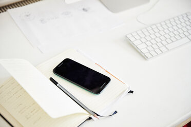 A desk with a computer and white keyboard, paperwork and a smart phone and pen. Overhead view. - MINF04605