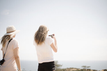 Woman and teenage girl with long blond hair standing outdoors, holding up a mobile phone, taking a picture. - MINF04606