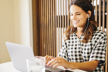 Woman with long brown hair, wearing a chequered shirt, working on a laptop computer. - MINF04615