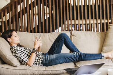 Woman with long brown hair lying on a sofa, using a mobile phone. - MINF04635