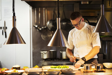 Chef standing in a restaurant kitchen, plating food. - MINF04653