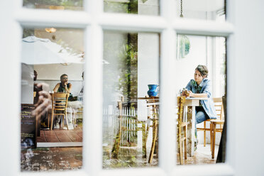 Blick durch ein Fenster in ein Café, Menschen sitzen an Tischen. - MINF04678