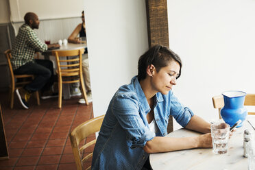 Frau mit kurzen braunen Haaren sitzt in einem Café und benutzt ein Mobiltelefon. - MINF04679