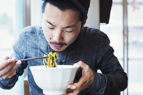 Ein Ramen-Nudel-Café in einer Stadt: Ein Mann sitzt und isst Ramen-Nudeln aus einer großen Schüssel mit Brühe. - MINF04694